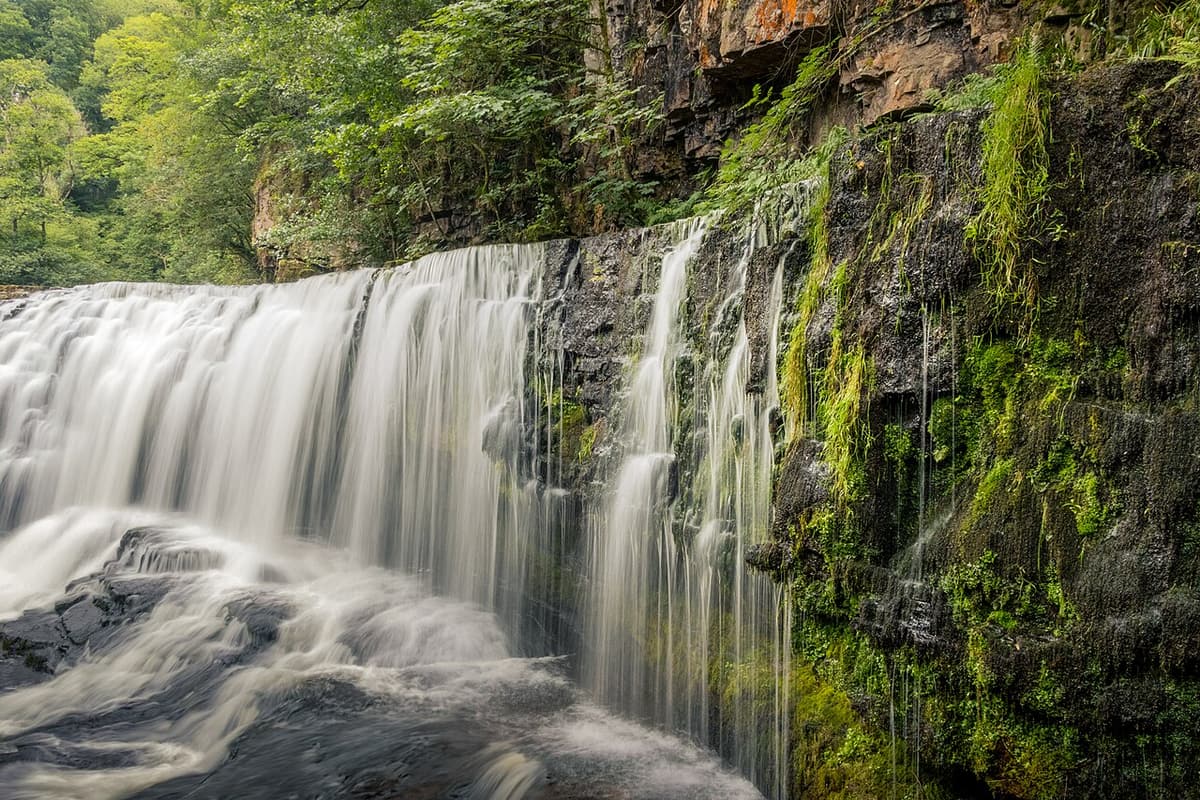 Ein breiter Wasserfall stürzt im Wald des Wasserfalllands über eine Felsstufe