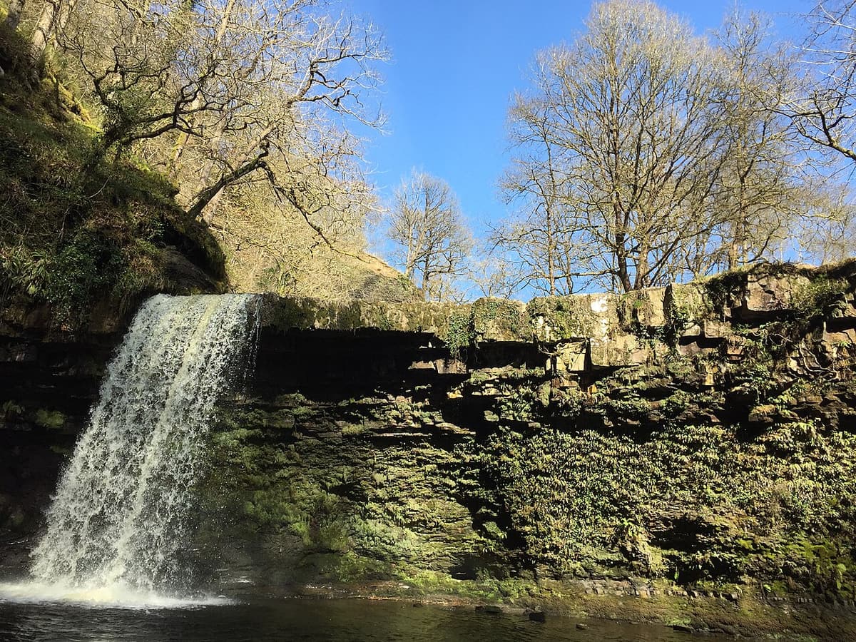 Ein Wasserfall mit Gumpe in einer engen, bewaldeten Schlucht bei Pontneddfechan